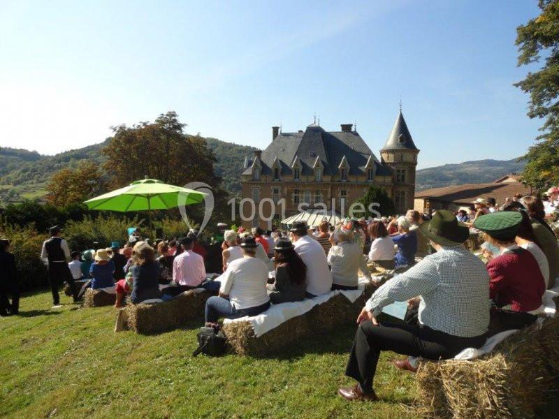 Un groupe de personnes assises sur des bottes de foin devant un château, lors d'un événement en plein air par temps…