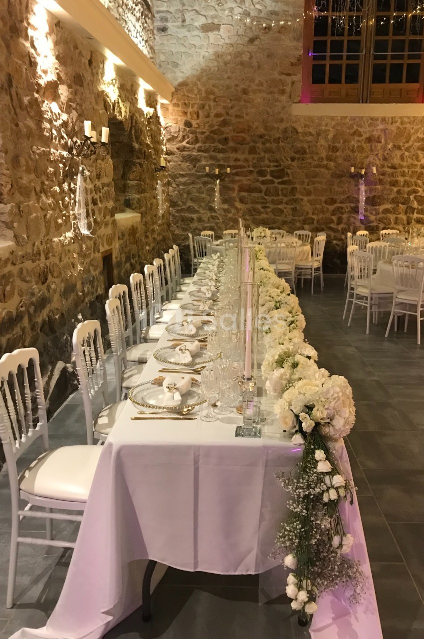 Table de réception élégamment décorée avec des fleurs blanches, dans une salle en pierre avec éclairage chaleureux.