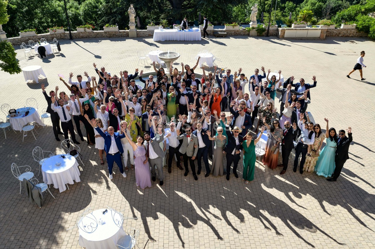 Groupe de personnes en tenue de cérémonie rassemblées sur une terrasse en plein air, levant les bras en signe de célébration.