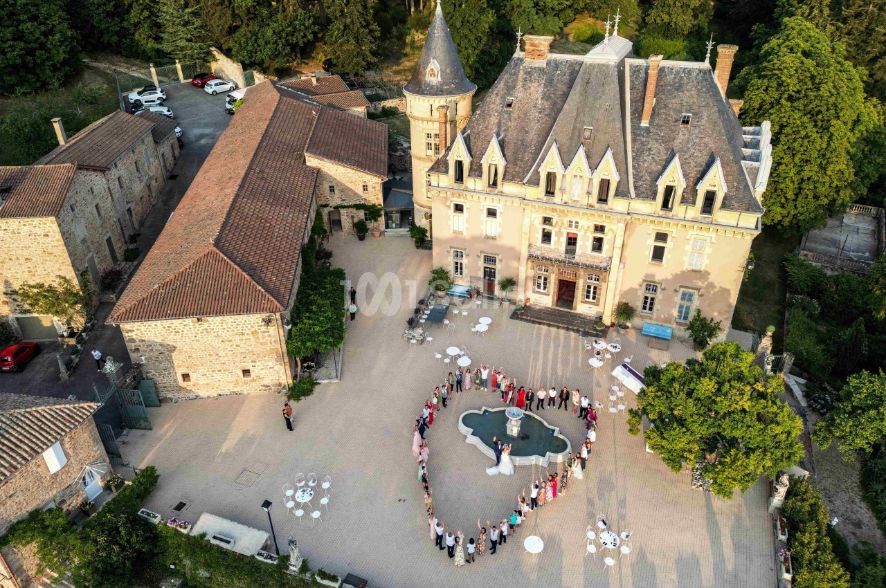 Vue aérienne d'un mariage dans la cour d'un château entouré de bâtiments anciens et de verdure.