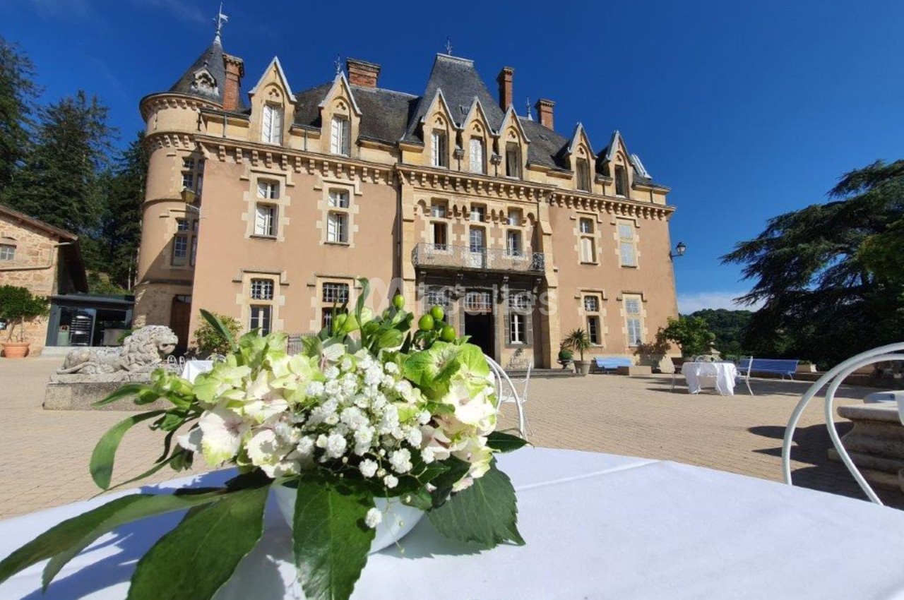 Vue d'un château en pierre avec des fleurs blanches au premier plan sur une table en extérieur.