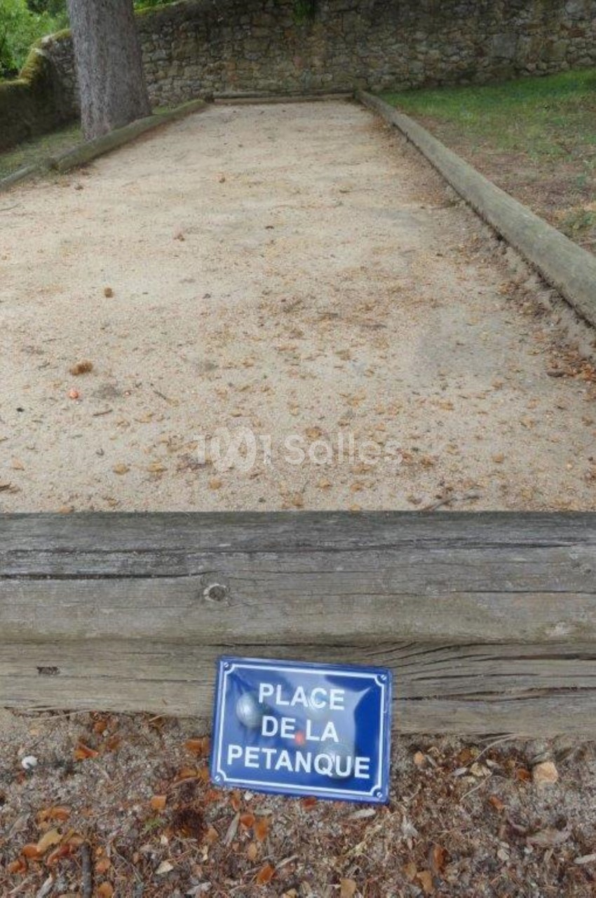 Terrain de pétanque en sable entouré de bordures en bois, avec un panneau indiquant ’Place de la pétanque’.