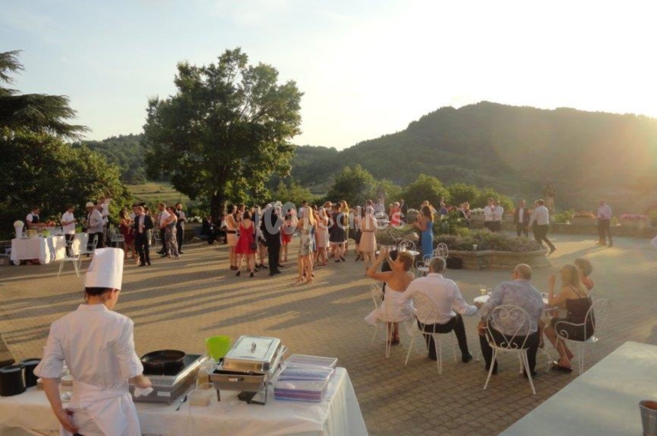 Groupe de personnes rassemblées en extérieur lors d'une réception au coucher du soleil, avec un chef cuisinant au premier…