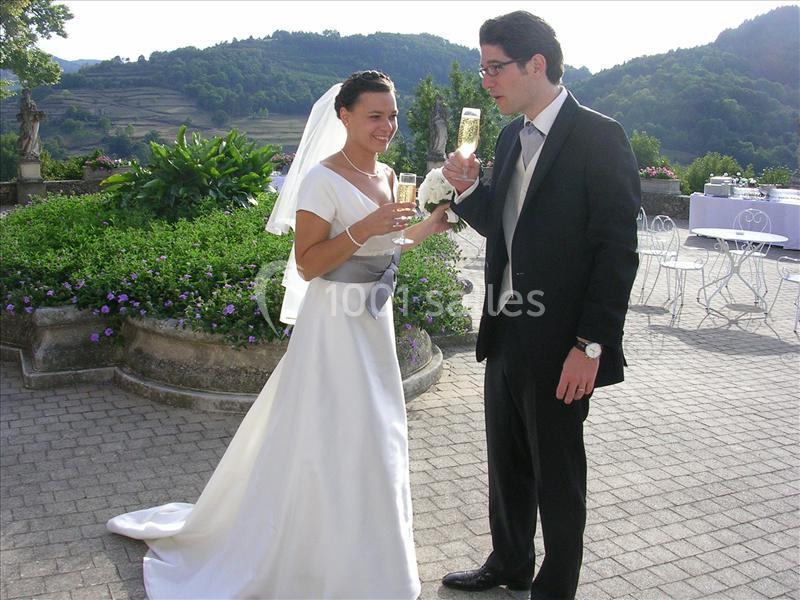 Un couple en tenue de mariage trinque avec des coupes de champagne dans un jardin avec vue sur des collines verdoyantes.