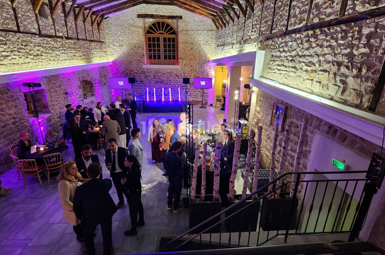 Personnes réunies dans une salle en pierre éclairée par des lumières colorées, discutant lors d'un événement.