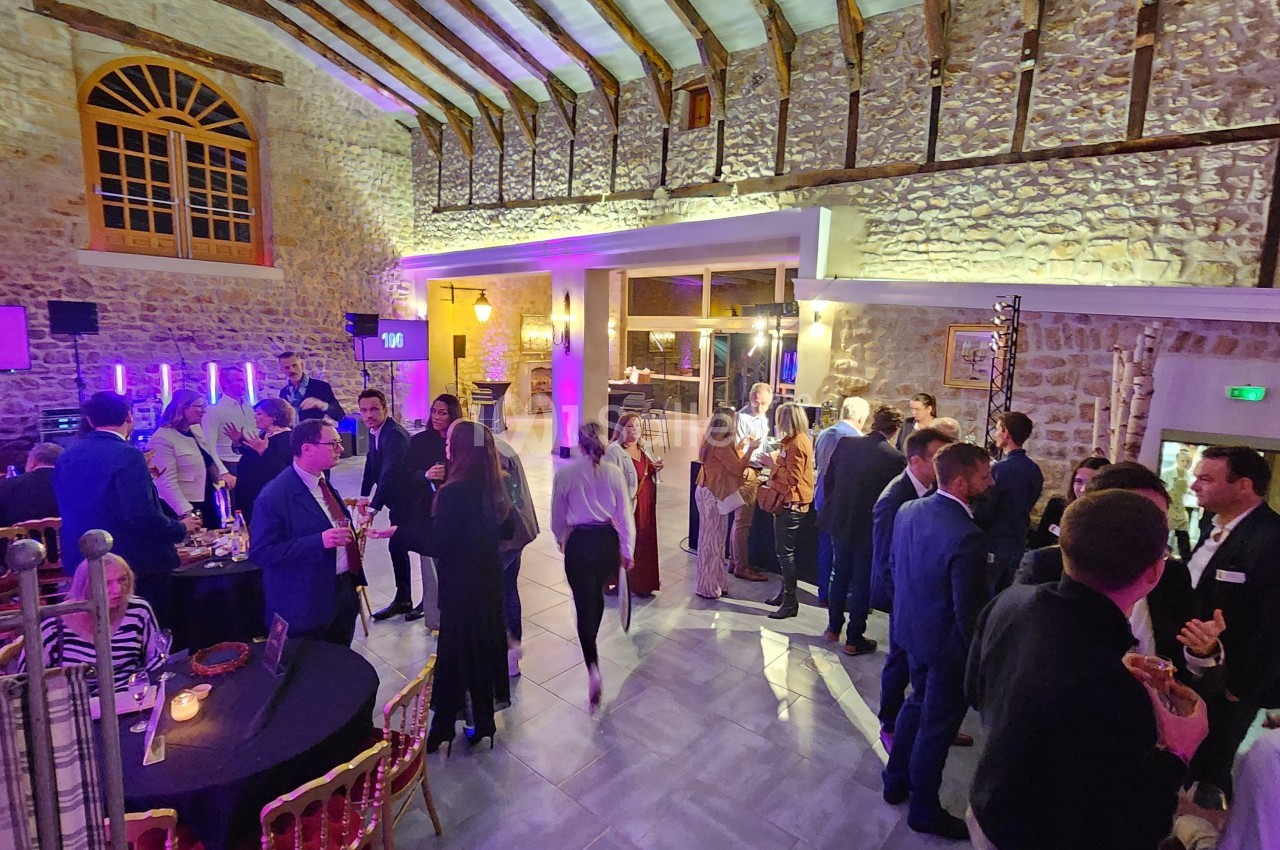 Des personnes discutent et se rassemblent dans une grande salle en pierre avec un éclairage chaleureux et des tables…