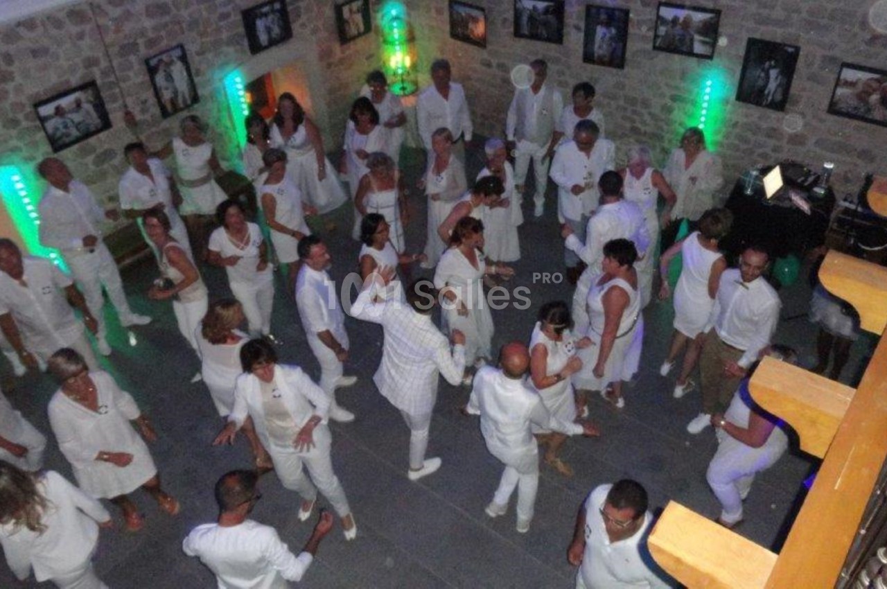 Personnes vêtues de blanc dans une salle en pierre, dansant sous des lumières colorées.