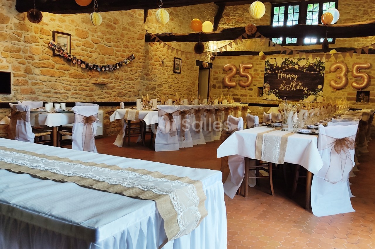 Salle décorée pour une fête d'anniversaire avec tables dressées, guirlandes et chiffres ’25’ et ’35’ en arrière-plan.