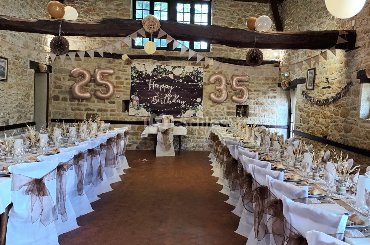 Salle décorée pour une fête d'anniversaire avec tables dressées, ballons ’25’ et ’35’ et une bannière festive.