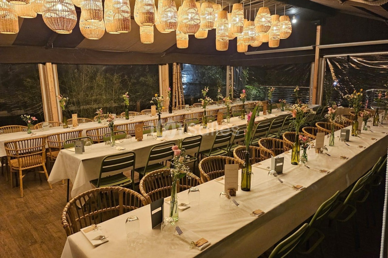Salle de réception avec longues tables dressées, décorées de fleurs et éclairées par des suspensions en osier.