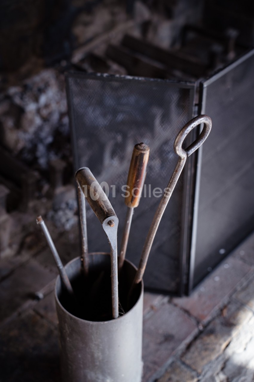 Outils en métal pour cheminée rangés dans un support cylindrique devant un pare-feu en métal.