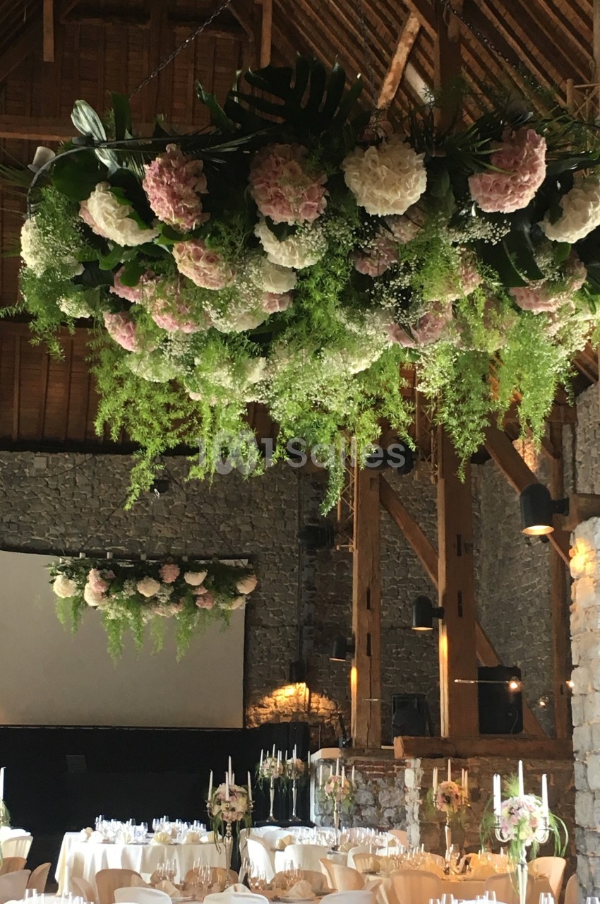 Décoration florale suspendue avec hortensias et feuillages dans une salle en pierre aménagée pour un événement.