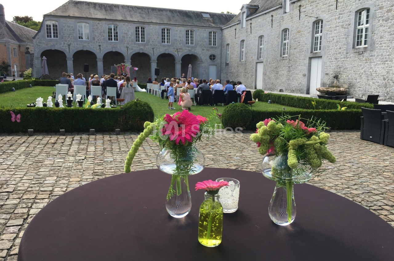 Table décorée avec des fleurs devant une cour pavée où se déroule une cérémonie en plein air.