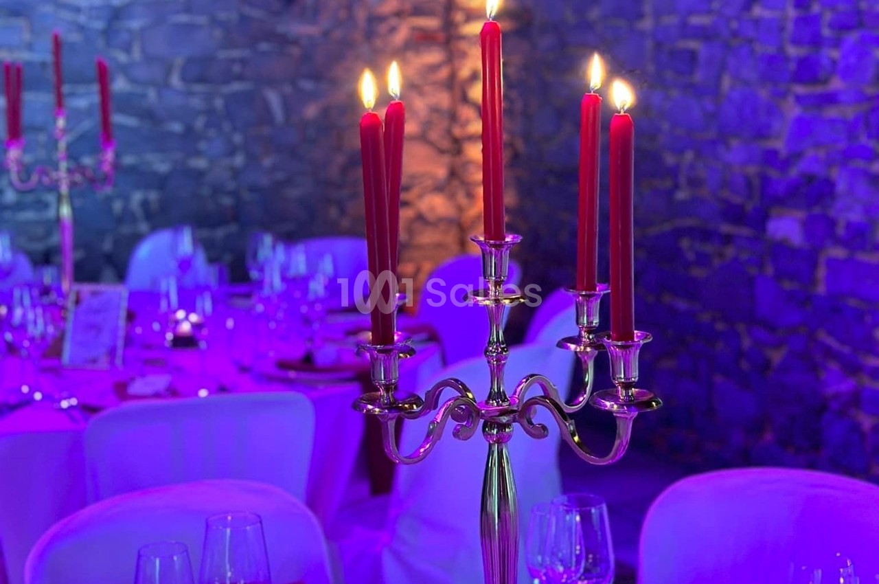 Chandelier argenté avec bougies rouges allumées, posé sur une table dressée dans une salle éclairée en lumière violette.