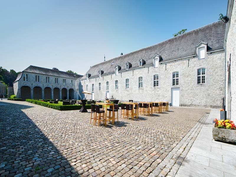 Cour pavée avec mobilier de terrasse en bois, entourée de bâtiments en pierre aux toits en ardoise.