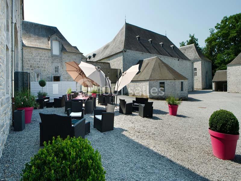 Cour pavée avec mobilier de jardin, parasols et pots de fleurs, entourée de bâtiments en pierre sous un ciel dégagé.
