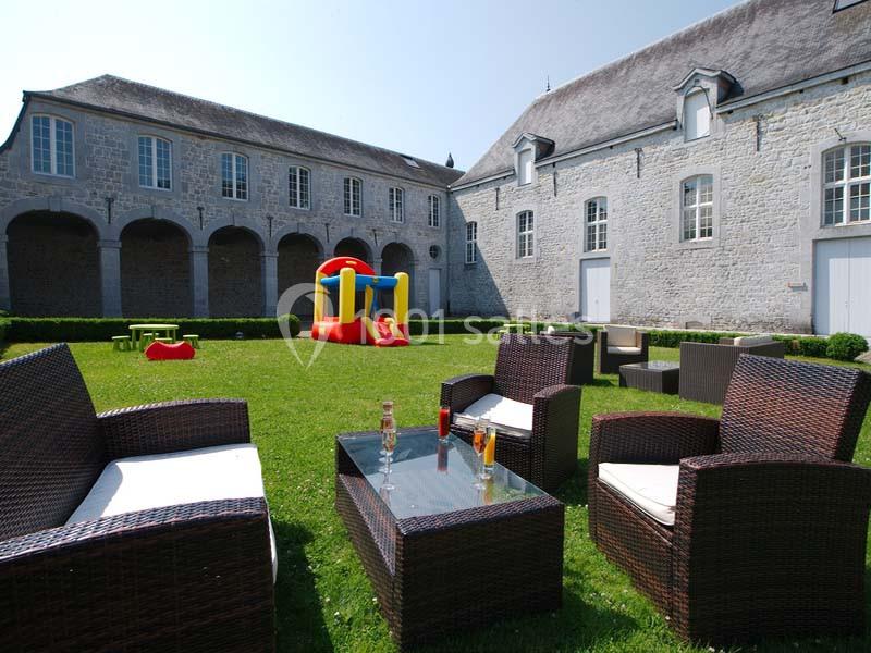 Mobilier de jardin en rotin sur une pelouse avec une structure gonflable colorée devant un bâtiment en pierre.
