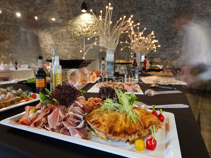 Plateau de charcuterie et pâté en croûte décoré de légumes, présenté sur une table de buffet dans une salle en pierre.
