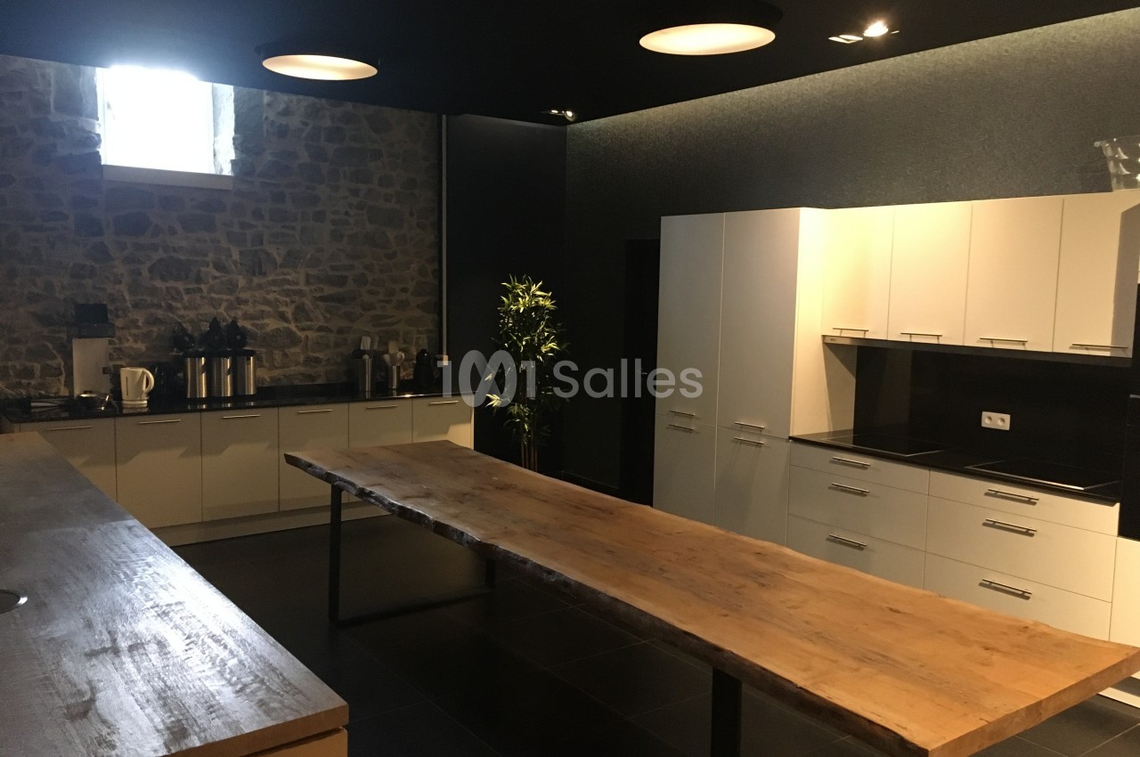 Cuisine moderne avec murs en pierre, éclairage tamisé, grand plan de travail en bois et rangements blancs.