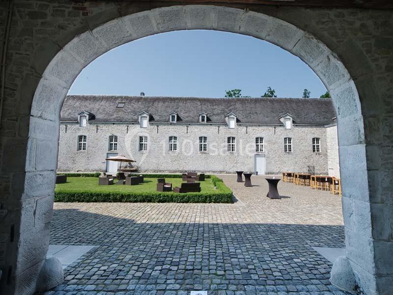 Cour intérieure pavée avec mobilier de jardin, entourée de bâtiments en pierre sous un ciel dégagé.