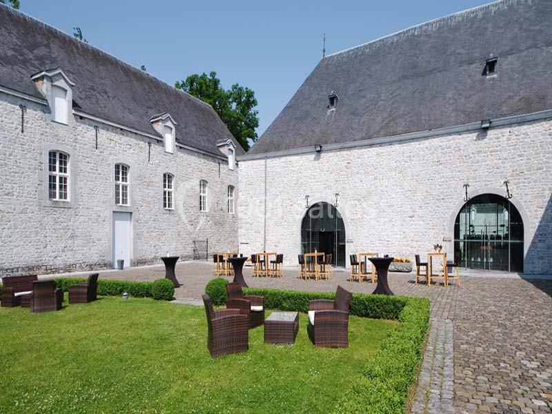 Cour intérieure pavée avec pelouse, mobilier de jardin en rotin et bâtiments en pierre aux toits d'ardoise.