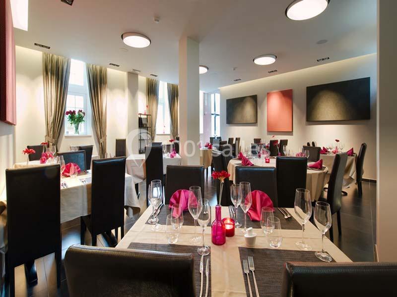 Salle de restaurant élégante avec tables dressées, nappes blanches, serviettes roses et lumière naturelle.