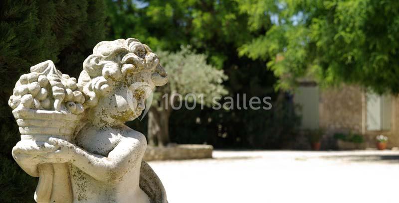 Statue en pierre représentant une figure féminine portant un panier, dans un jardin ensoleillé avec des arbres en arrière…