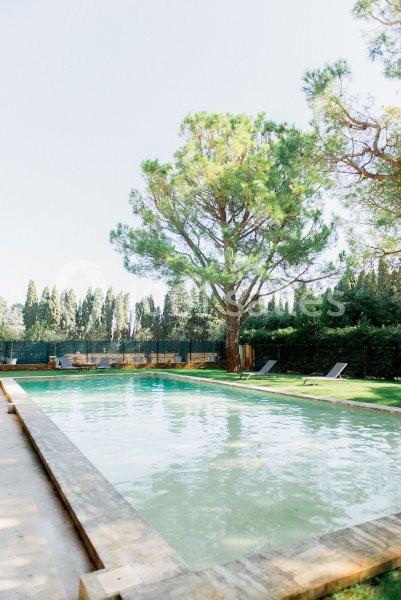 Piscine extérieure entourée d'arbres et de chaises longues dans un cadre verdoyant.