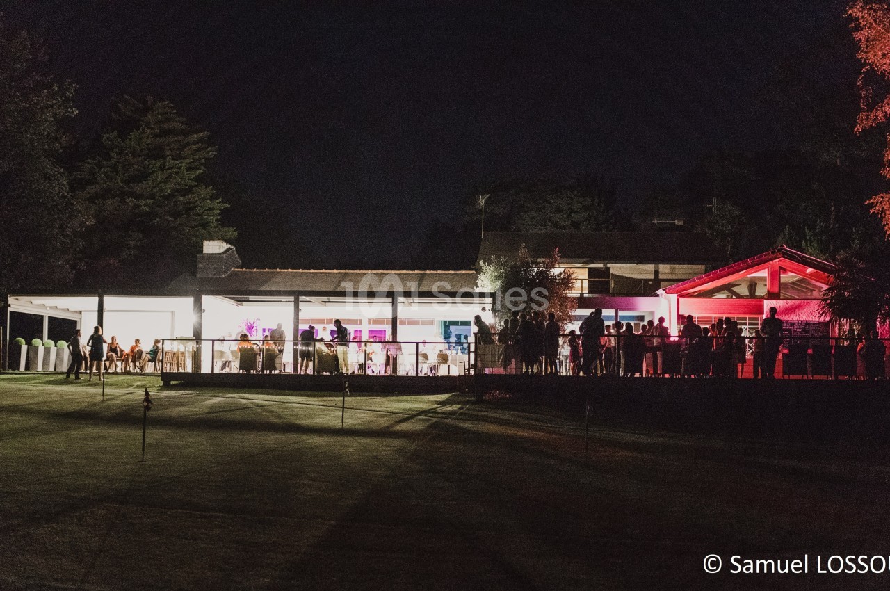 Vue nocturne d'un bâtiment éclairé avec des lumières colorées, entouré de personnes et d'un espace extérieur sombre.