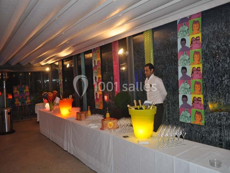 Un buffet avec des seaux de boissons, des verres alignés et un serveur dans une salle décorée de portraits colorés.