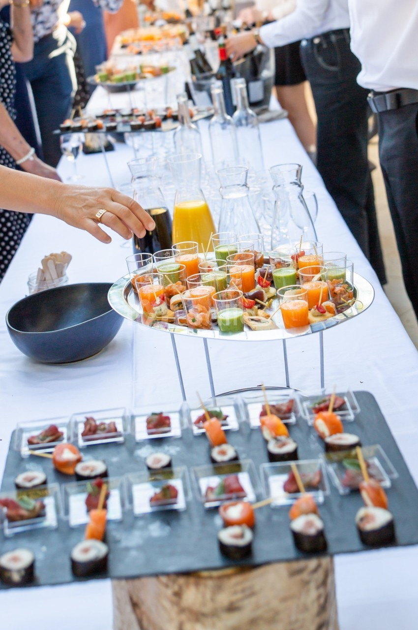 Buffet avec verrines colorées, amuse-bouches variés et boissons, disposé sur une table blanche lors d'un événement.