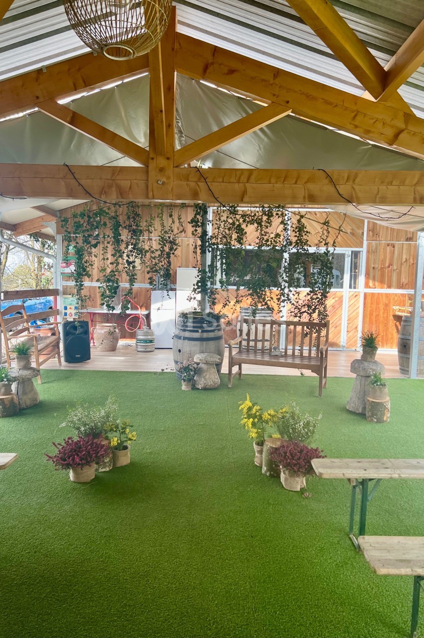 Espace extérieur couvert avec toit en bois, bancs, plantes décoratives et sol en gazon synthétique.