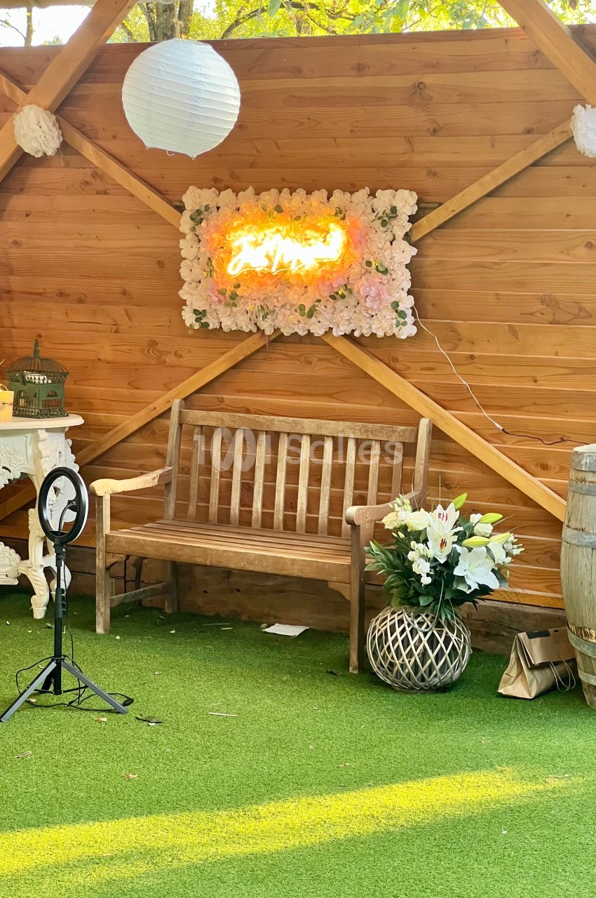Banc en bois devant un mur en bois décoré de fleurs, d'une enseigne lumineuse et d'éléments de décoration.