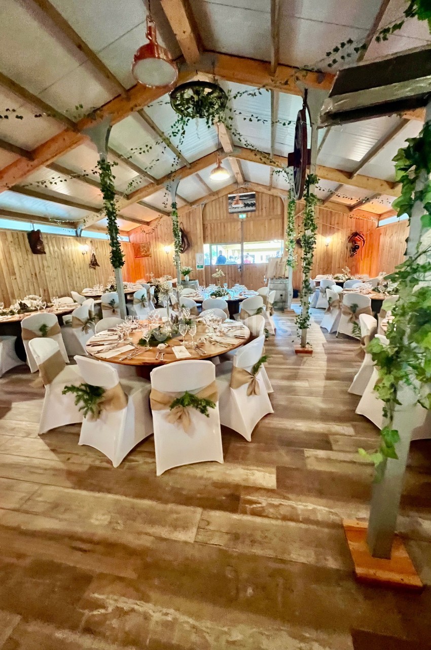 Salle de réception décorée avec des tables rondes, nappes blanches, chaises habillées et guirlandes végétales suspendues.