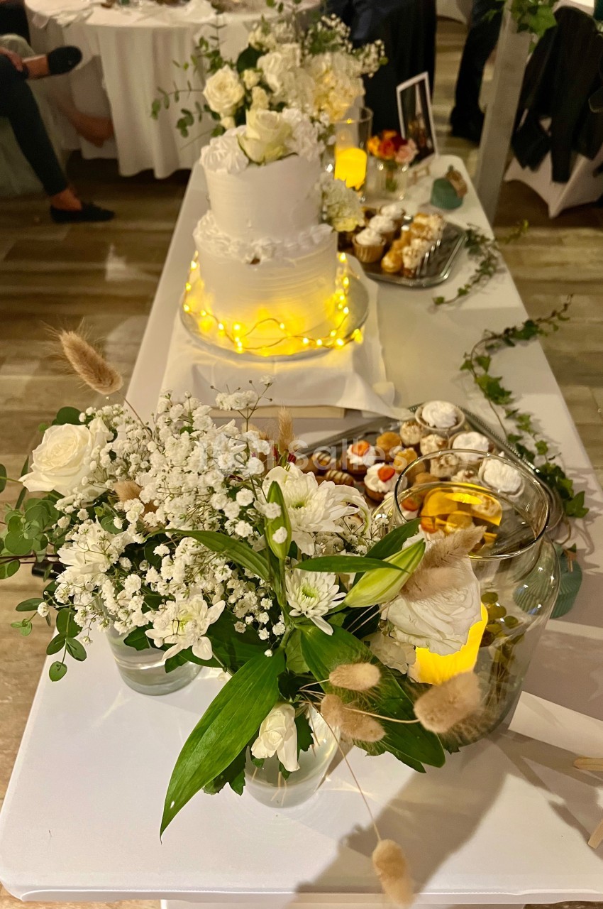 Table décorée pour un mariage avec un gâteau blanc à étages, fleurs blanches et un assortiment de desserts.