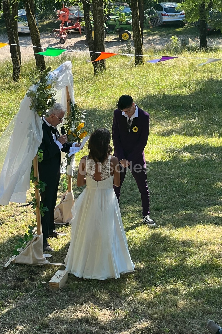 Un couple se tient devant un officiant lors d'une cérémonie de mariage en plein air, entouré de verdure.