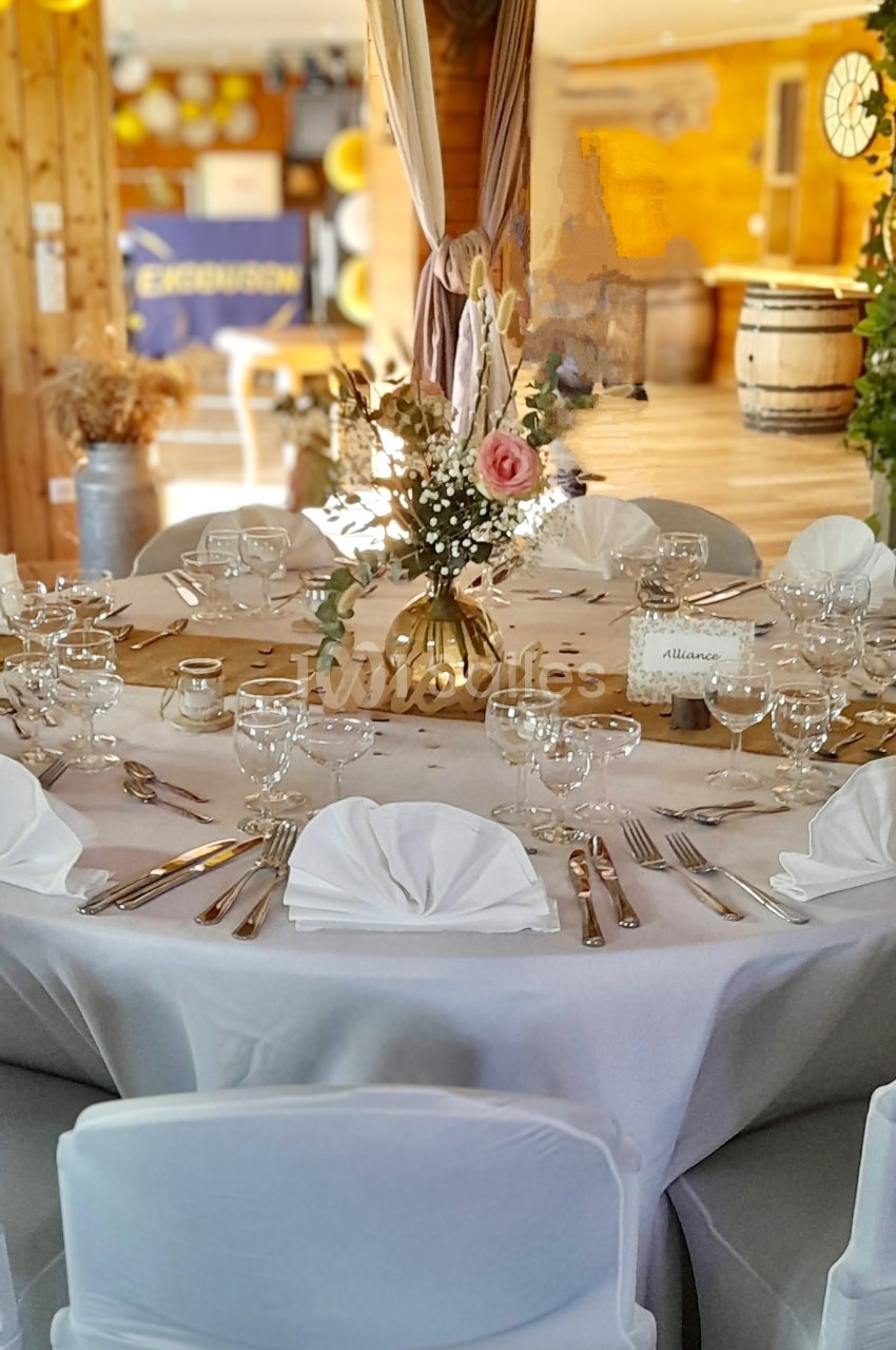 Table ronde décorée pour un événement, avec nappes blanches, vaisselle élégante et centre de table floral.