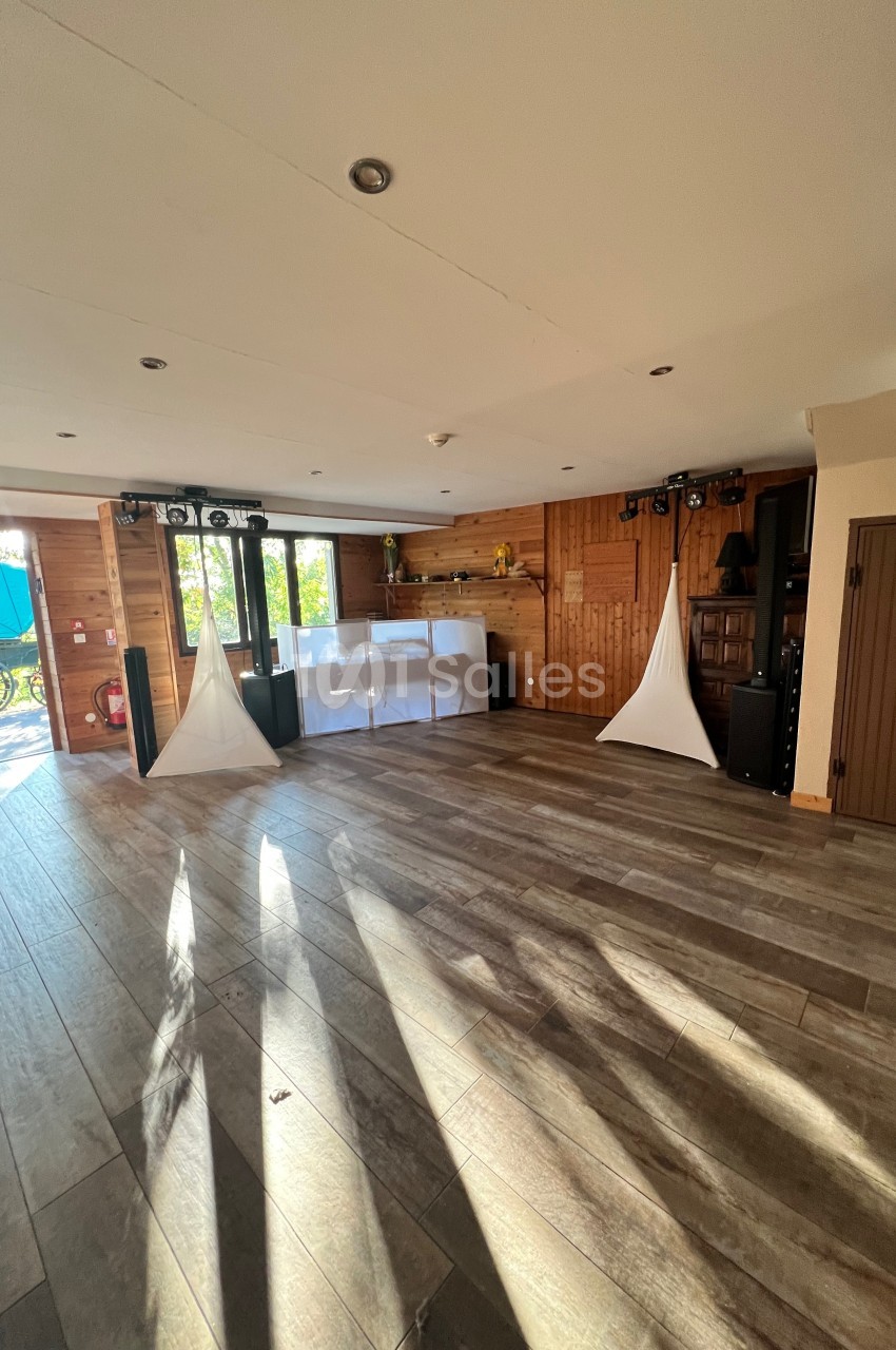Salle en bois lumineuse avec parquet, équipements audio, décorations blanches et vue sur l'extérieur par des portes vitrées.