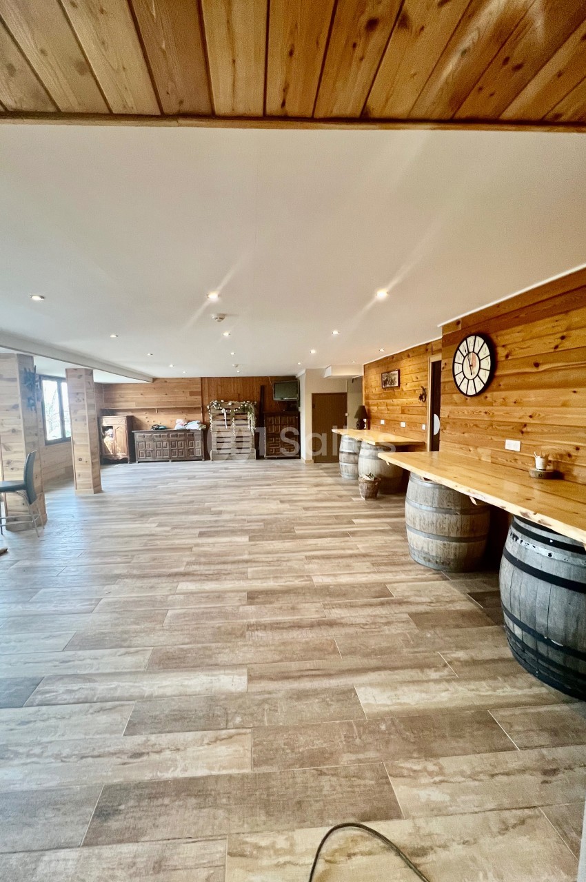 Salle spacieuse avec sol en bois clair, murs en bois, bar en arrière-plan et tonneaux décoratifs.