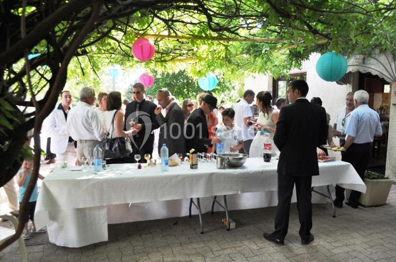 Groupe de personnes rassemblées autour d'une table dressée pour un buffet en extérieur sous une pergola décorée.