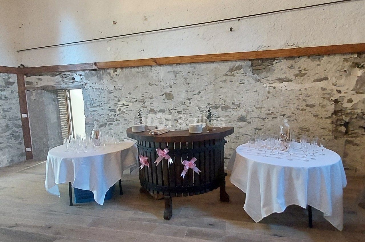 Salle en pierre avec deux tables rondes dressées pour un événement, décorées de nappes blanches et rubans roses.