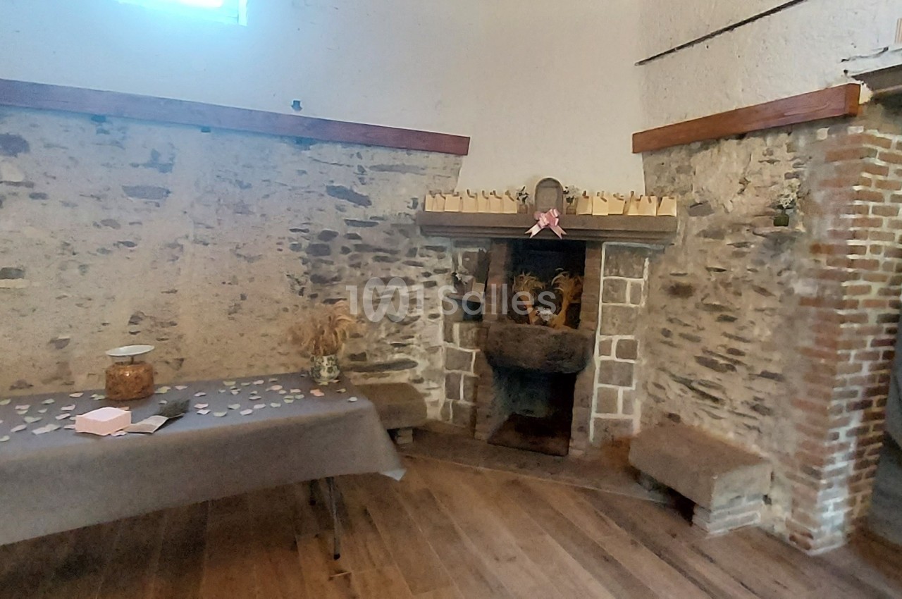 Salle rustique avec murs en pierre, cheminée décorée et table recouverte d'une nappe grise avec des objets disposés.