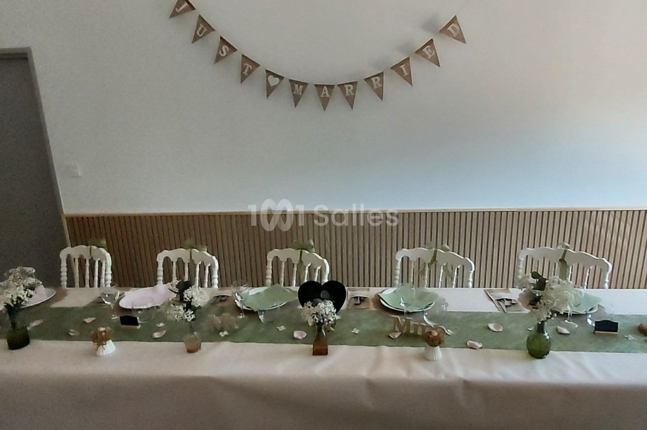 Table décorée pour un événement, avec nappes blanches, chemins de table verts, vaisselle et ornements floraux.