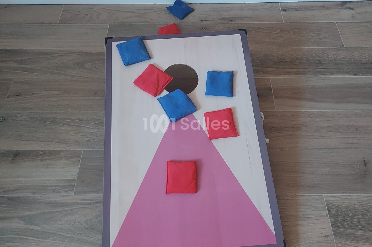 Planche de jeu de lancer avec des sacs en tissu rouges et bleus, posée sur un sol en bois.
