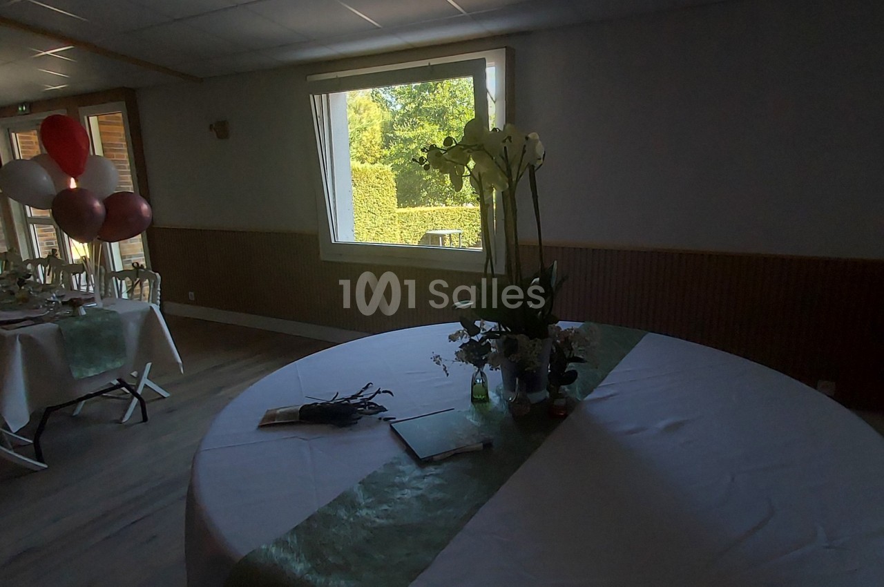 Salle de réception avec une table ronde décorée, des ballons et une grande table dressée en arrière-plan.