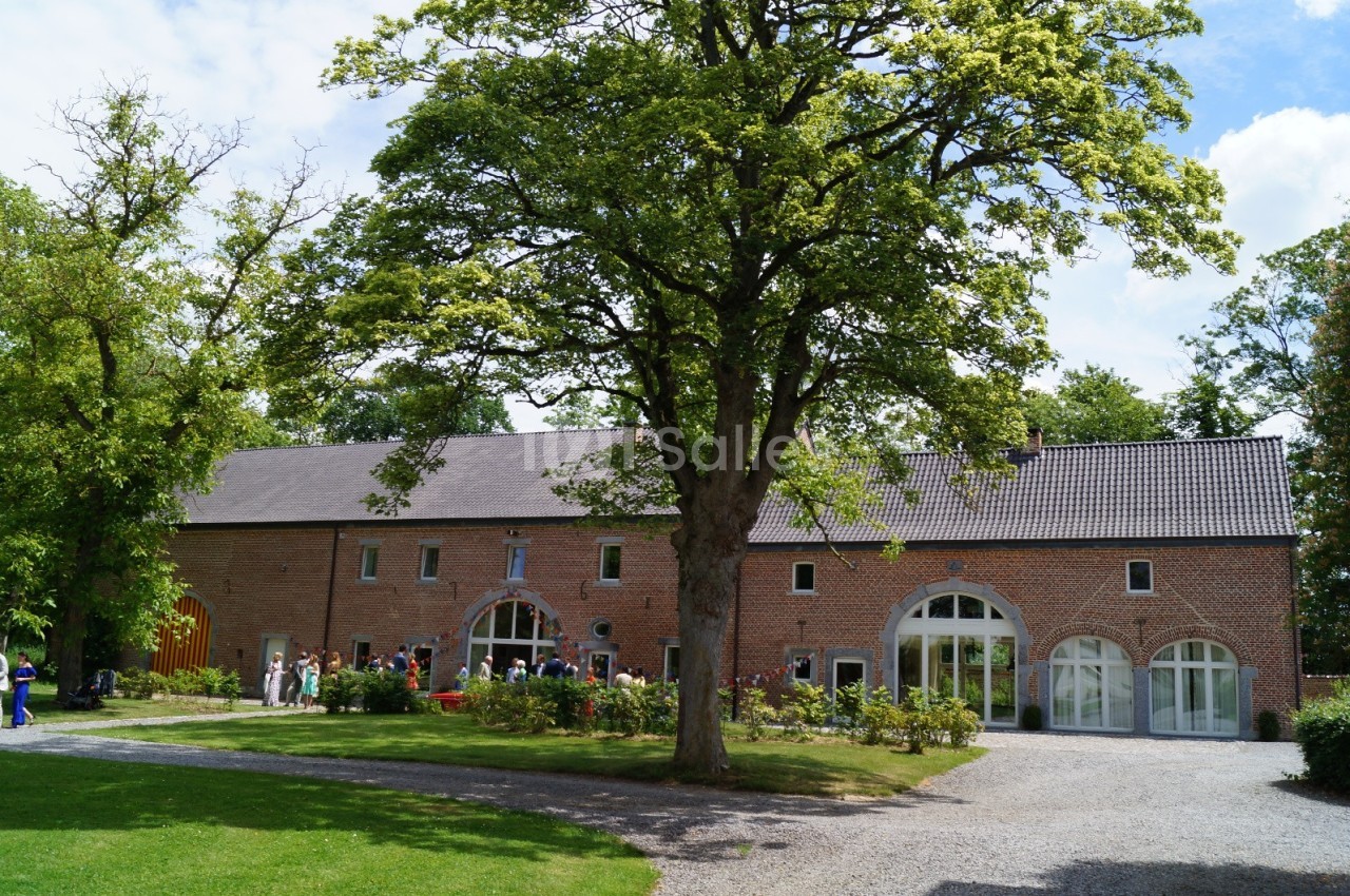 Bâtiment en briques rouges avec grandes fenêtres cintrées, entouré d'arbres et d'une pelouse sous un ciel dégagé.