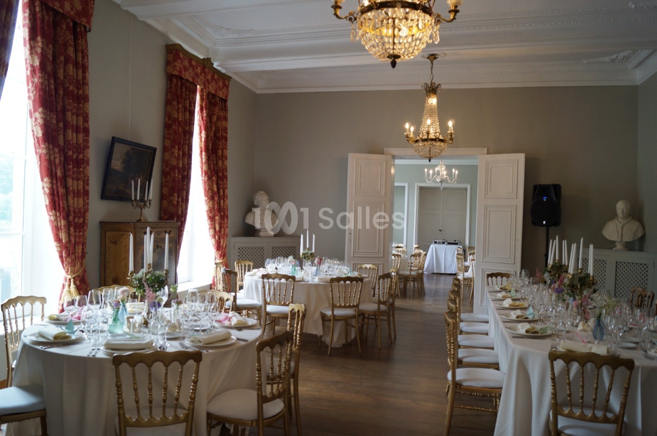 Salle élégante décorée pour un repas, avec tables dressées, chaises dorées et lustres en cristal.