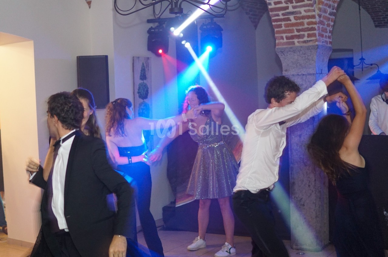 Des personnes dansent sous des lumières colorées dans une salle avec des murs en briques et des arches en pierre.