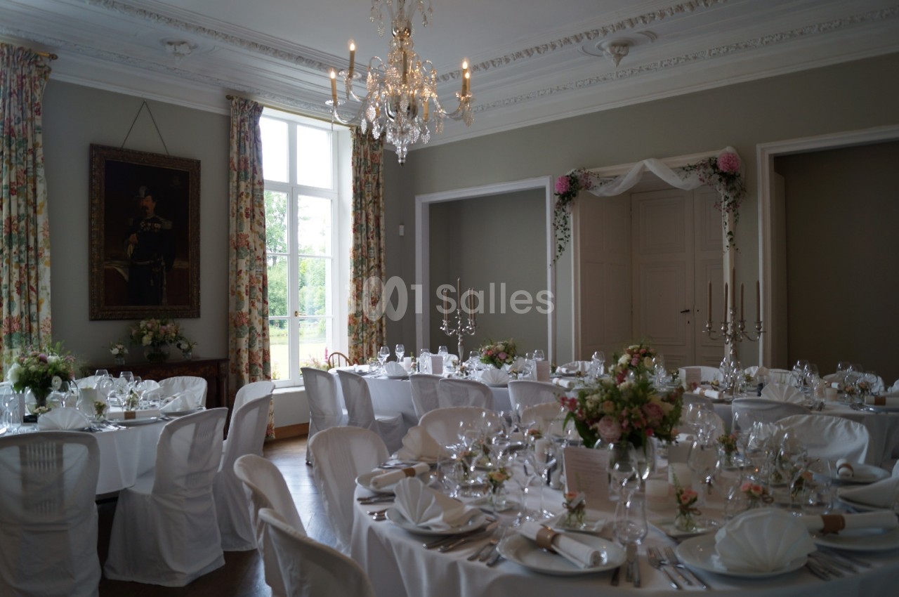 Salle élégante décorée pour un mariage, avec tables dressées, nappes blanches, chandeliers et fleurs.