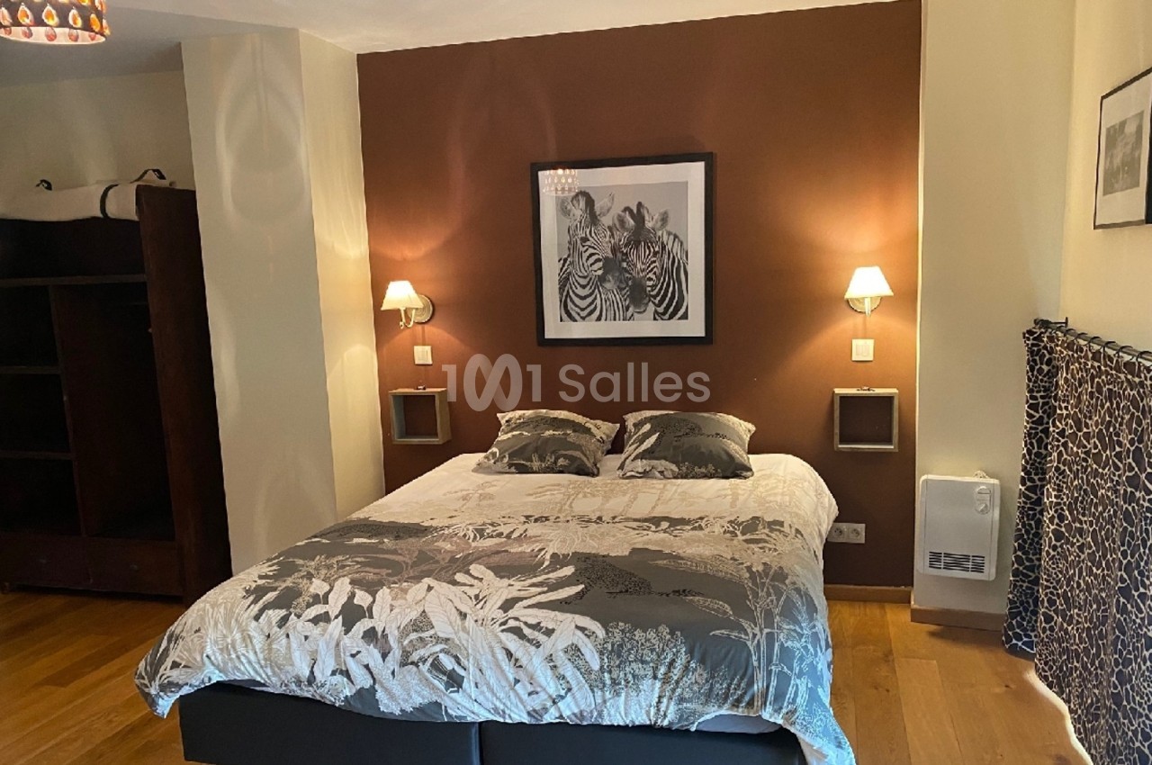 Lit double avec housse à motifs végétaux, encadré par deux appliques murales, dans une chambre au mur brun décoré.